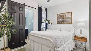 Una camera da letto con un letto, un comodino, una lampada, un quadro, una ventola a soffitto e una porta.