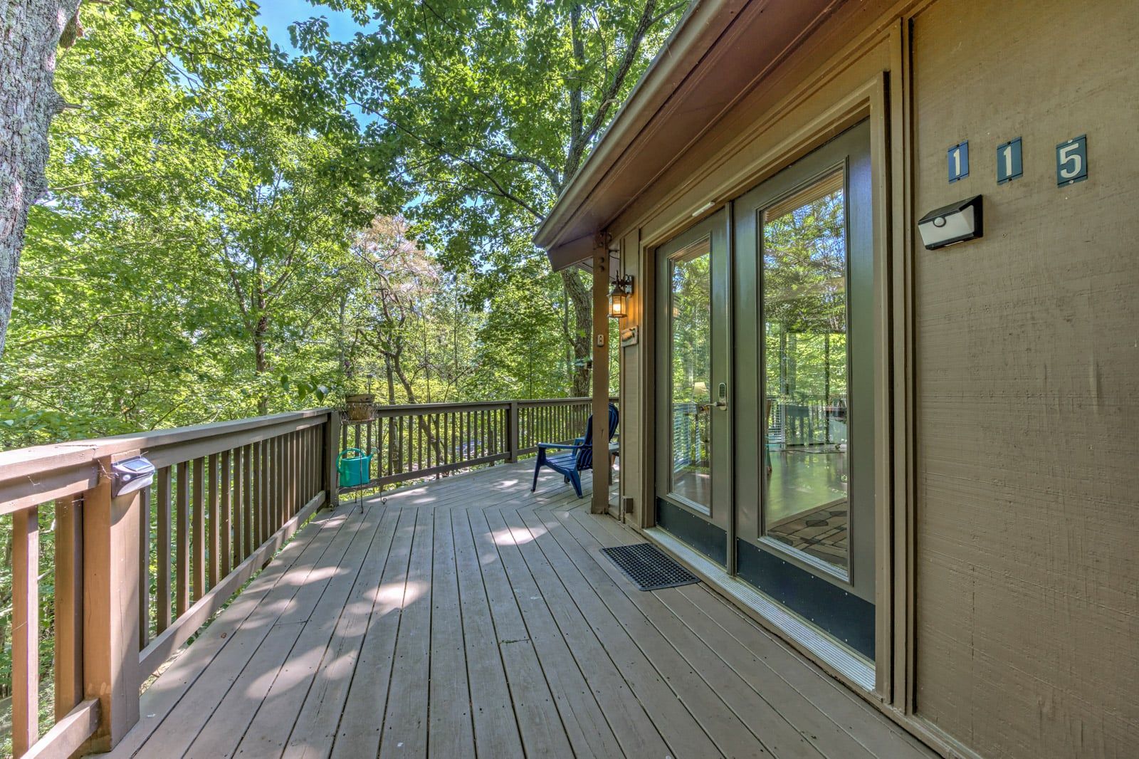 A wooden deck with a glass door leading to a covered area, surrounded by trees.