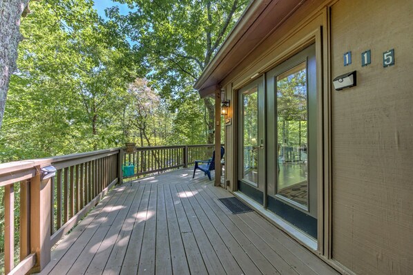 A wooden deck with a glass door leading to a covered area, surrounded by trees.