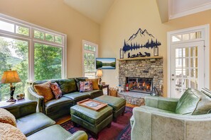 A cozy living room with a stone fireplace, leather sofas, and a large window overlooking greenery. - Bear Bluff - Game Room, Fire Table, Comfy Patio + Community Activities (Jasper)