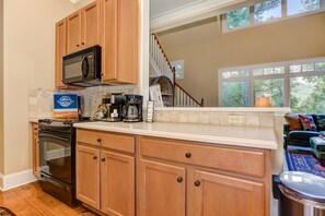 A kitchen with wooden cabinets, a microwave, a coffee maker, and a sign for vacation rentals. - Bear Bluff - Game Room, Fire Table, Comfy Patio + Community Activities (Jasper)