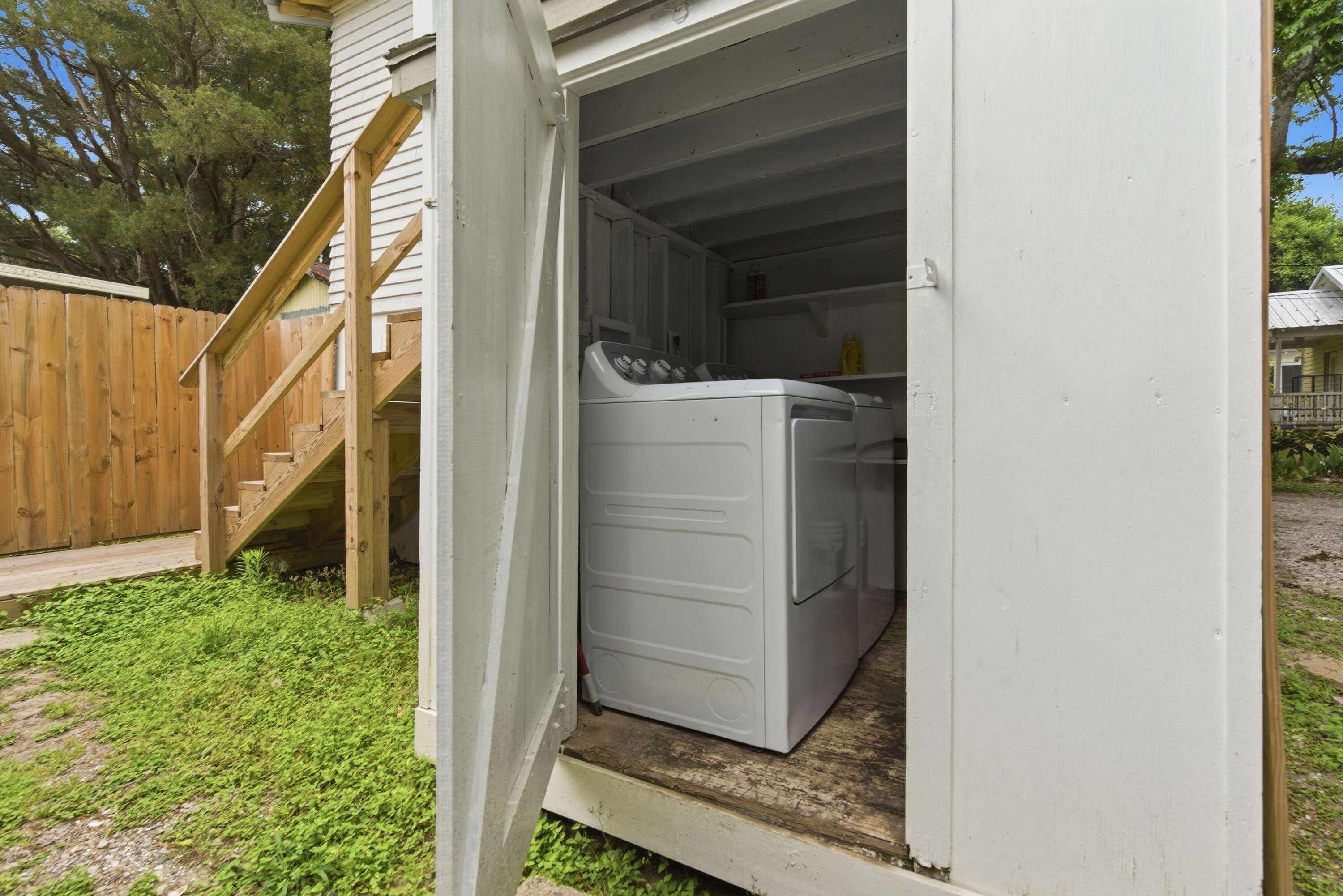 A laundry room with a washing machine and dryer, a wooden staircase, and a fenced yard.