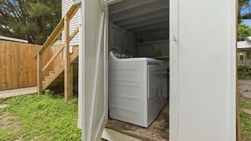 A laundry room with a washing machine and dryer, a wooden staircase, and a fenced yard.