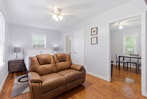 Uma sala de estar moderna com um sofá de couro marrom, um ventilador de teto e uma área de jantar com mesa e cadeiras.