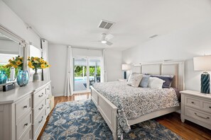 Un dormitorio con cama, mesitas de noche, cómoda y ventilador de techo, con vista a un balcón.