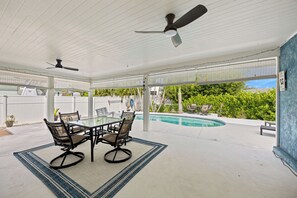 Eine Außenpatio mit Glastisch und Stühlen, einem Deckenventilator und Blick auf einen Swimmingpool.