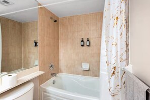 A modern bathroom with a bathtub, a shower, and a toilet. There are two wall-mounted soap dispensers and a towel rack. - Stylish 2+1 Condo | Views Near SQ1 Mall (Mississauga)