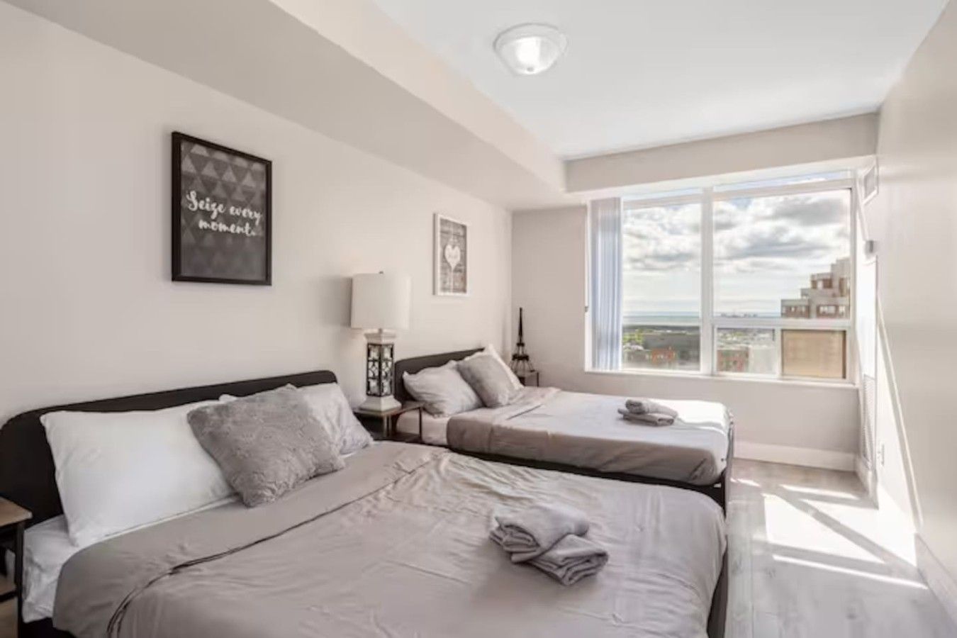 A hotel room with two beds, a large window, and a city view.