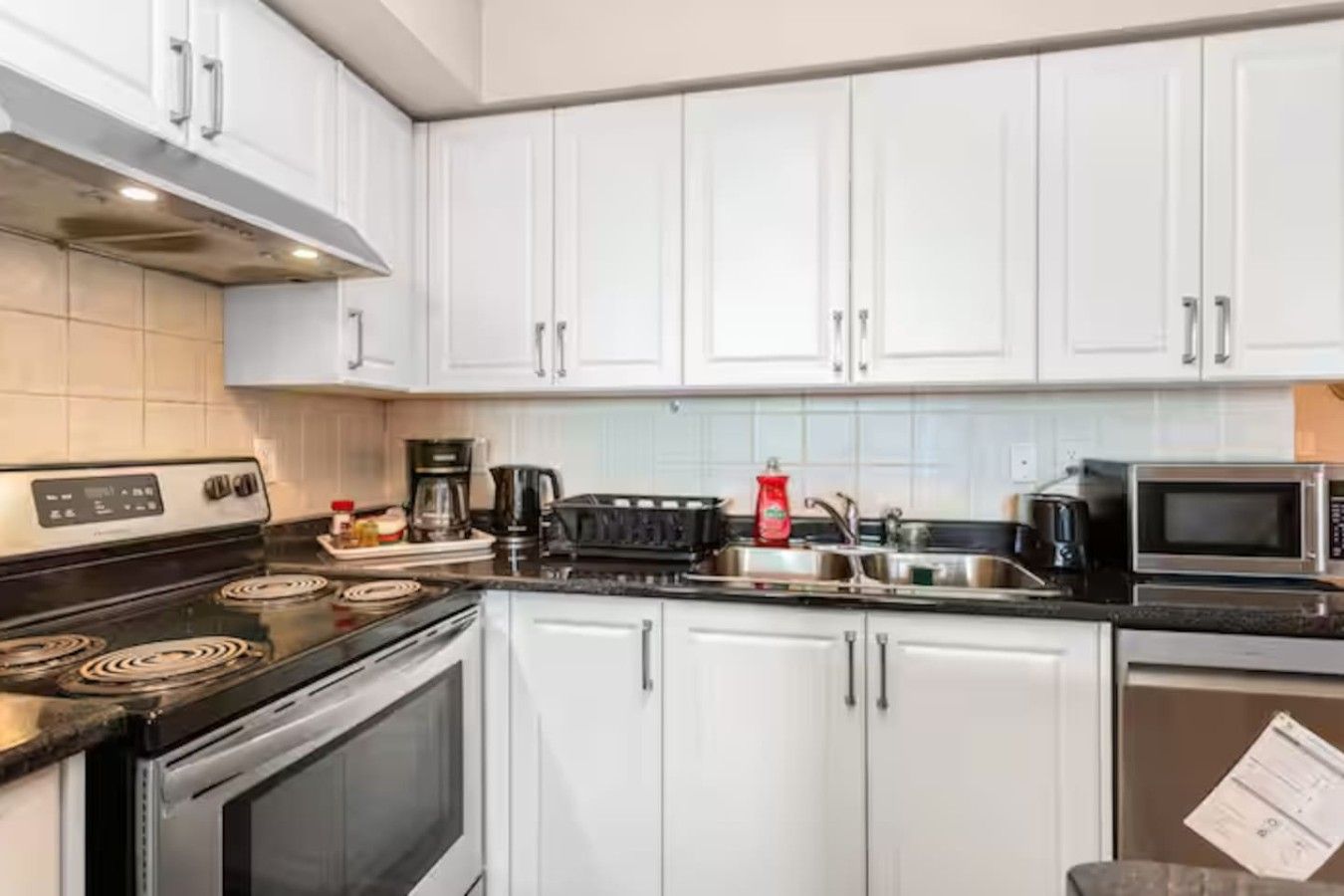 A kitchen with white cabinets, a stove, a microwave, and a coffee maker.