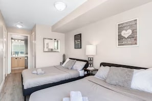 A hotel room with two beds, a mirror, a bedside table with a lamp, and a framed quote on the wall. - Stylish 2+1 Condo | Views Near SQ1 Mall (Mississauga)