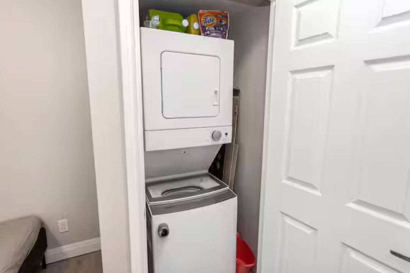 A compact laundry area with a washing machine and dryer, a small shelf with detergent, and a red trash bin.