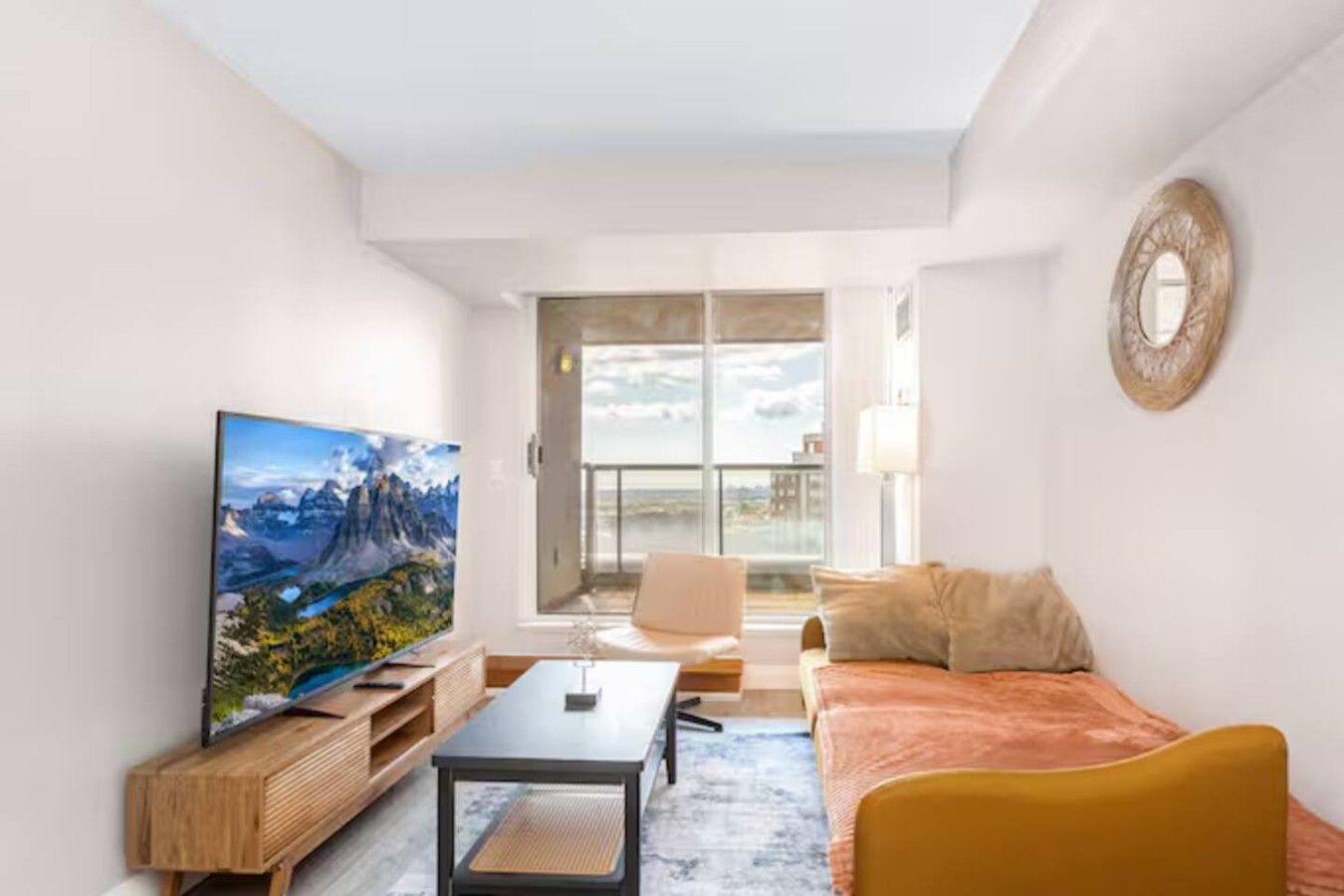 A modern living room with a television, a sofa, a coffee table, and a view of the outdoors.