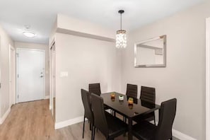 A dining area with a table and chairs, a chandelier, and a mirror on the wall. - Stylish 2+1 Condo | Views Near SQ1 Mall (Mississauga)