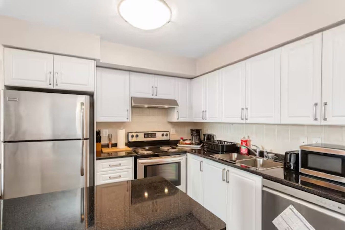 A modern kitchen with white cabinets, stainless steel appliances, and a granite countertop.