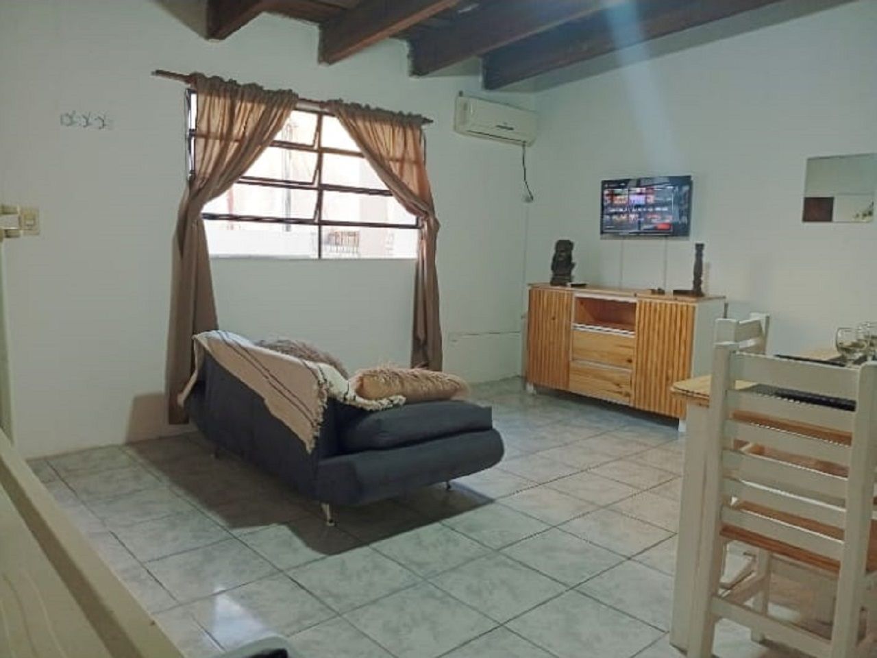 Una habitación con cama, televisión, aparador de madera y ventana con cortinas.