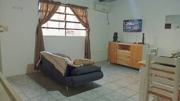 Una habitación con cama, televisión, aparador de madera y ventana con cortinas.