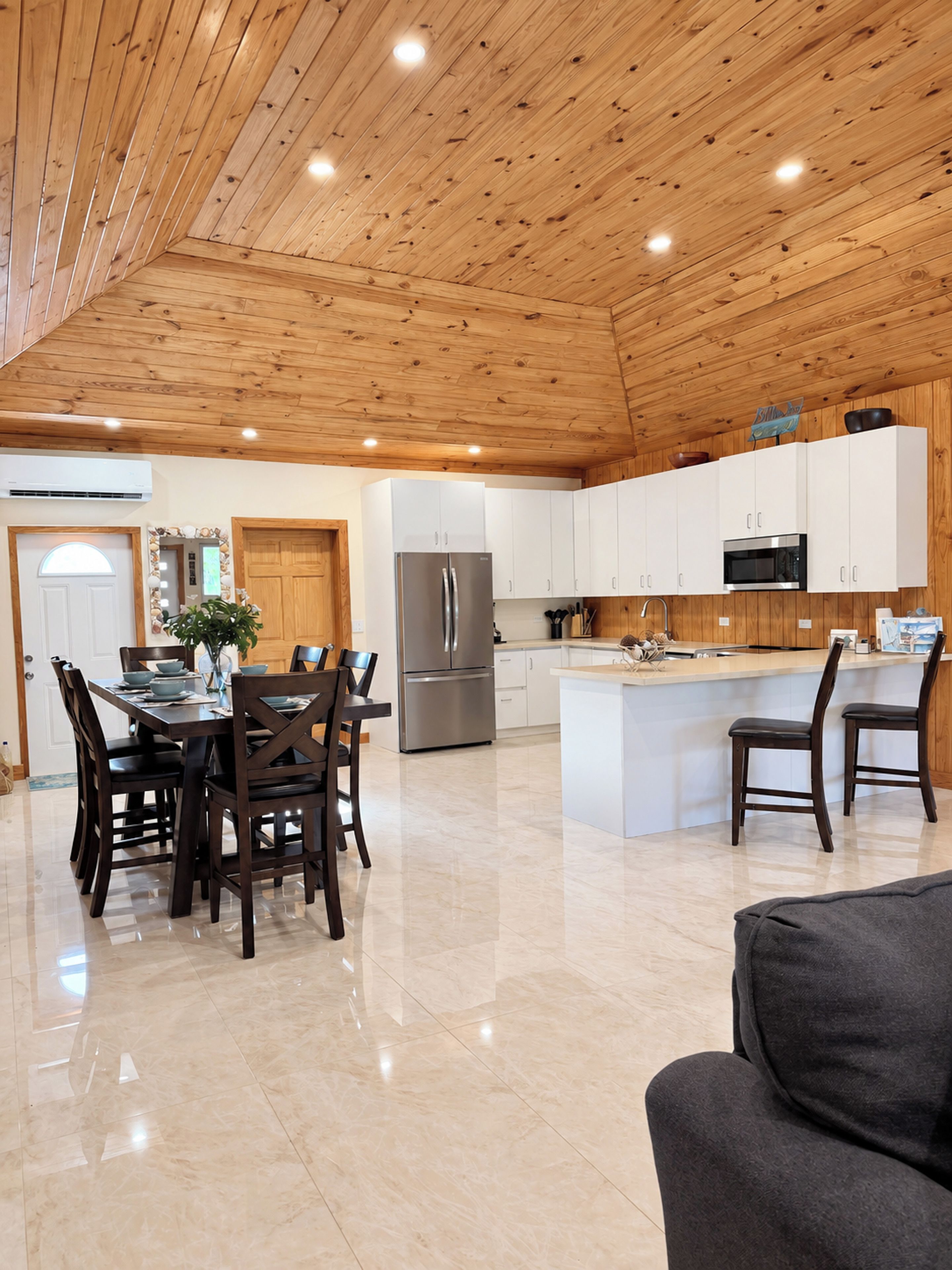 A spacious kitchen with wooden ceiling, white cabinets, a stainless steel refrigerator, and a central island with seating.