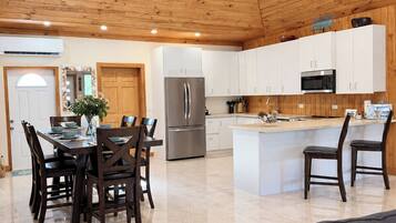 A spacious kitchen with wooden ceiling, white cabinets, a stainless steel refrigerator, and a central island with seating.