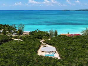 A coastal property with a swimming pool, surrounded by dense greenery and a clear view of the ocean.