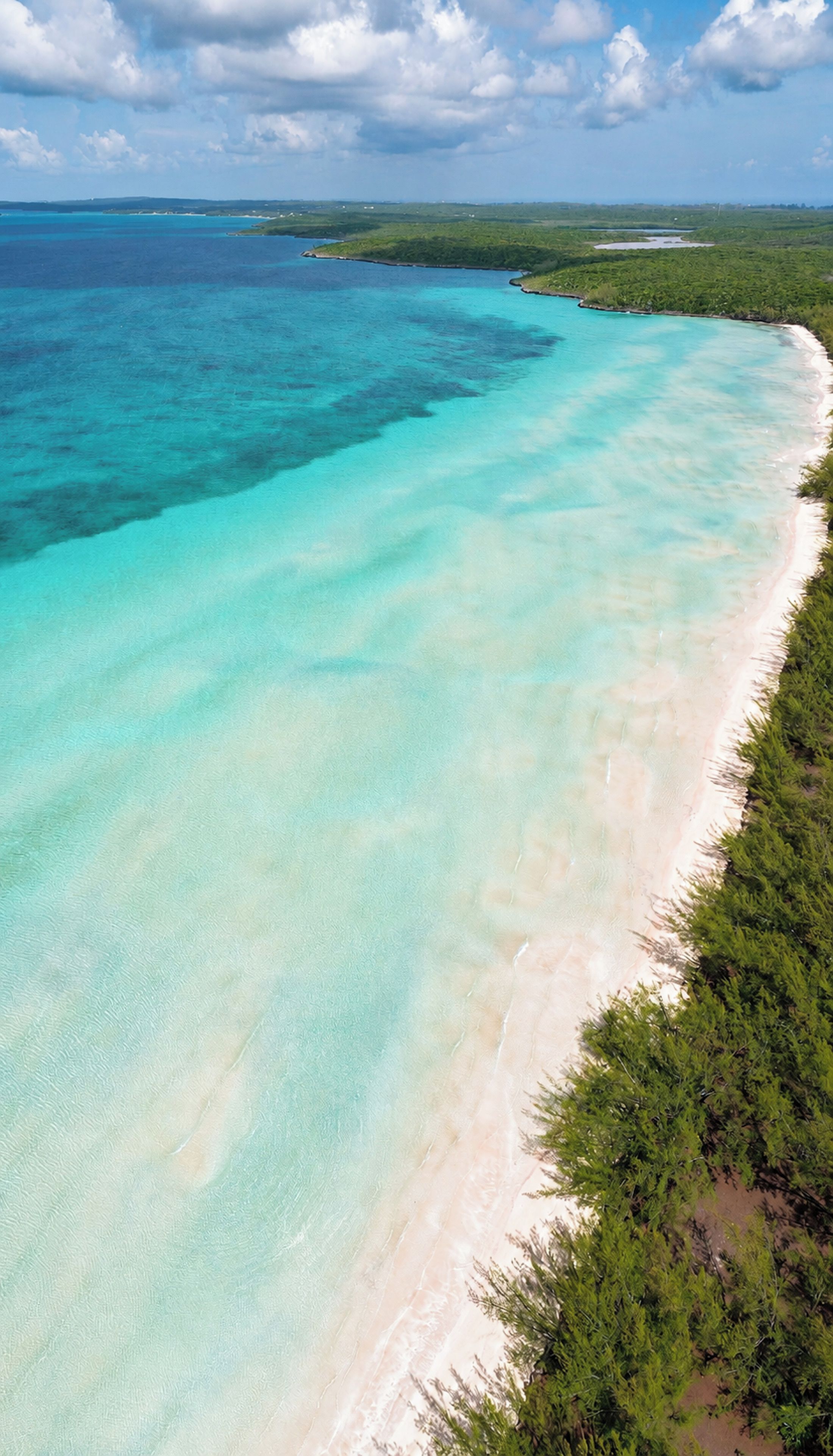 A coastal landscape with clear turquoise waters and a sandy beach.