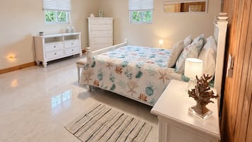 Ein Schlafzimmer mit Holzbalkendecke, einem Bett mit floralem Überwurf, einem Nachttisch, einer Kommode und zwei Fenstern mit Jalousien.