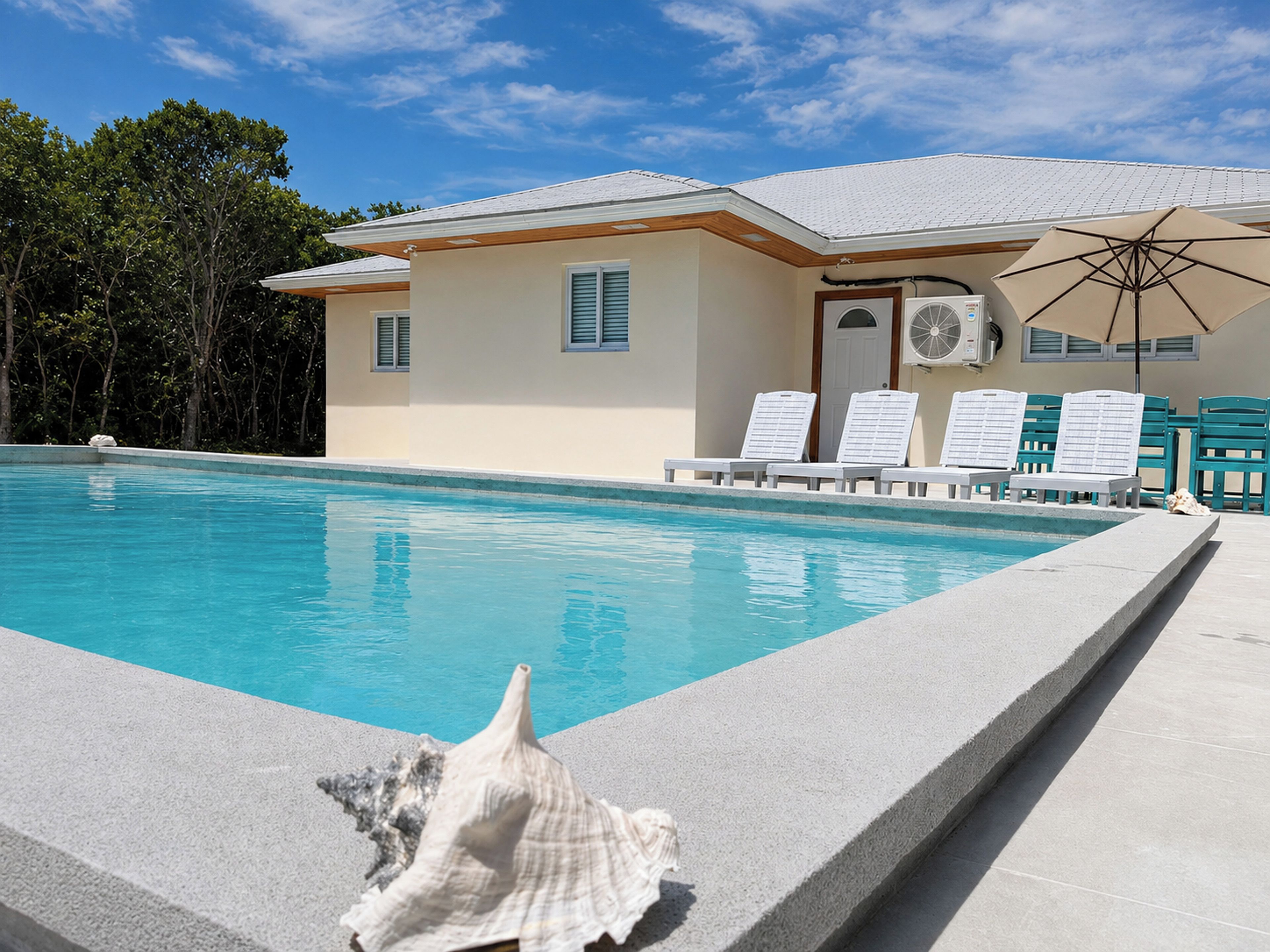 A swimming pool with lounge chairs and an umbrella, surrounded by a building with a tiled roof.