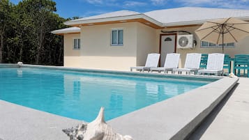 A swimming pool with lounge chairs and an umbrella, surrounded by a building with a tiled roof.