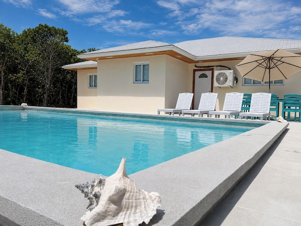 A swimming pool with lounge chairs and an umbrella, surrounded by a building with a tiled roof.