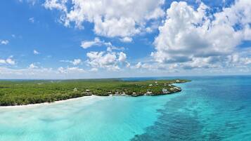 An aerial view of a tropical island with clear turquoise waters, dense green vegetation, and scattered buildings.