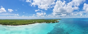 An aerial view of a tropical island with clear turquoise waters, dense green vegetation, and scattered buildings.