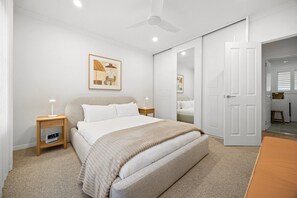 A bedroom with a bed, bedside tables, a ceiling fan, a door, and a framed picture on the wall. - Luna—Canopy Views from a Peaceful Garden Haven (College Park)