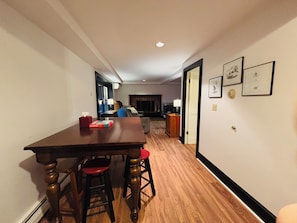 Un comedor con mesa de madera y taburetes, chimenea y cuadros en la pared.