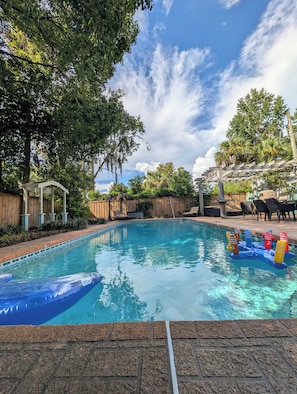 Una piscina con cubierta de madera, rodeada de árboles y una pérgola.