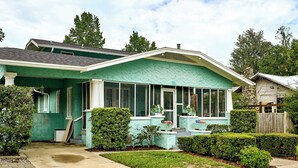 Uma casa térrea com fachada verde e varanda coberta.