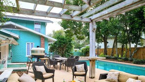 Área de varanda coberta com móveis de exterior, piscina e casa com fachada azul.