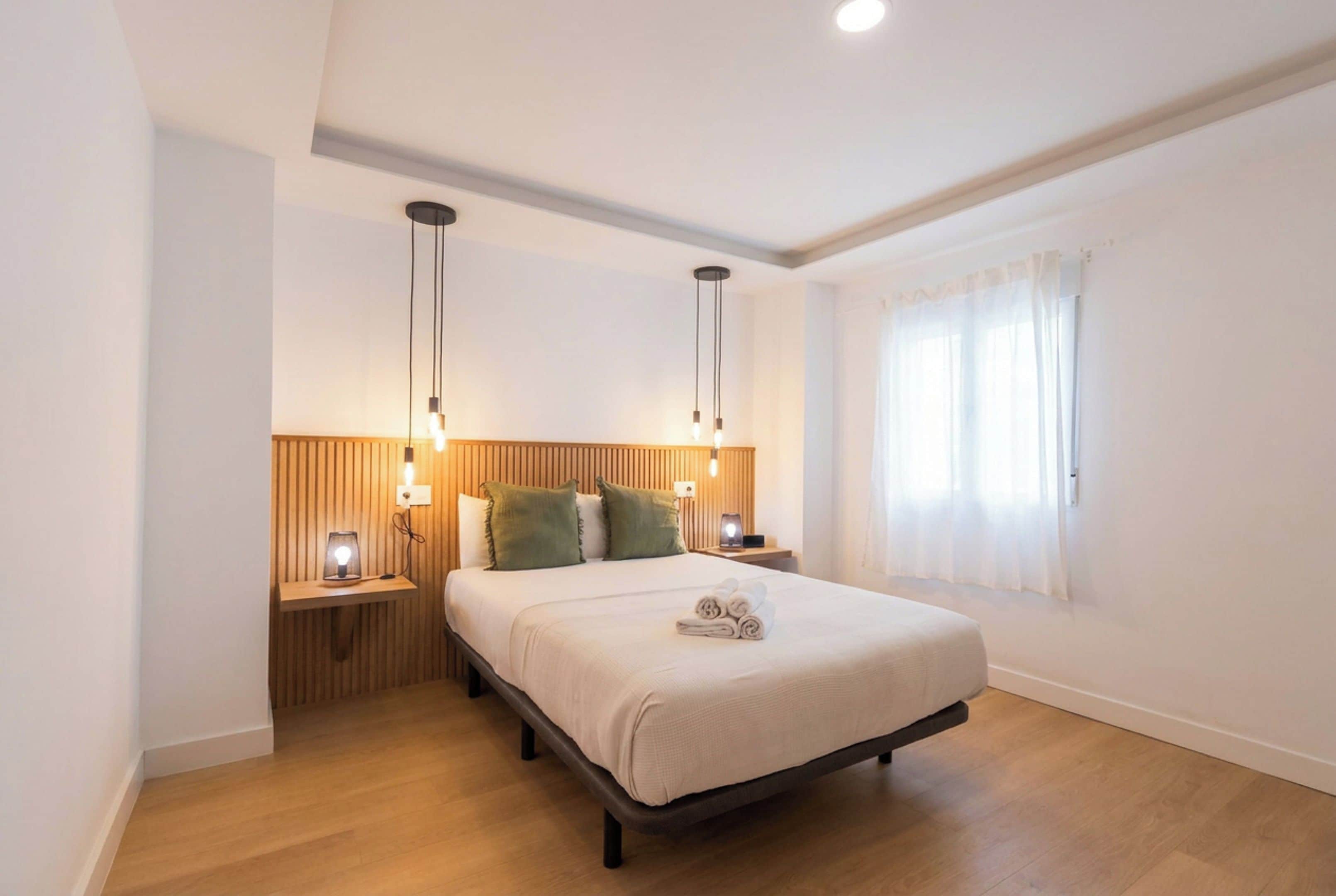 A hotel room with a bed, wooden headboard, bedside lamps, and a window with curtains.