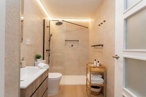 Ein kleines Badezimmer mit Dusche, Toilette und Ablage für Pflegeprodukte.