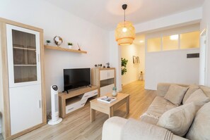 A modern living room with a flat-screen TV, wooden furniture, a standing fan, and a sofa. - Elegant Stay La Naval 2 (Las Palmas de Gran Canaria)
