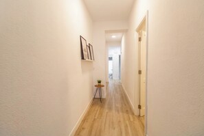 A narrow hallway with a wooden floor, white walls, and a small table with a plant. - Elegant Stay La Naval 2 (Las Palmas de Gran Canaria)