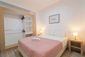 Ein Hotelzimmer mit Bett, Schrank, Nachttisch mit Lampe und Wand mit einem gerahmten Schild.