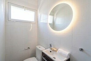 A modern bathroom with a toilet, sink, and a round mirror with built-in lighting. - Elegant Stay La Naval 3 (Las Palmas de Gran Canaria)