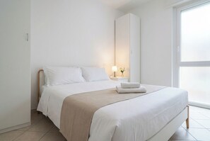 A minimalist hotel room with a bed, bedside table, lamp, and a view of the outside. - Elegant Stay La Naval 3 (Las Palmas de Gran Canaria)