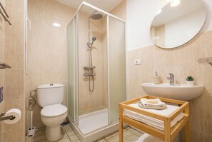 Ein modernes Badezimmer mit einer Duschkabine, Toilette, Waschbecken und einem Holzregal mit Handtüchern.
