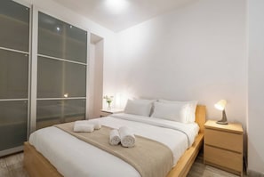 Une chambre moderne avec un grand lit, une table de chevet avec une lampe et une porte-fenêtre coulissante.