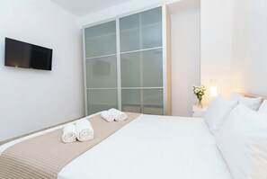 A hotel room with a bed, a flat-screen TV, a sliding glass door, and a bedside table with a vase of flowers. - Elegant Stay La Naval 4 (Las Palmas de Gran Canaria)