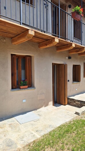 A building with a balcony, wooden beams, a window with a potted plant, and a door. - I Sitoù - Feoun Apartment - the warmth of the fireplace (Ostana)