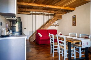 A kitchen with a modern stove, a red sofa, and a dining table with white chairs. - I Sitoù - Ratizin Apartment: The Scent of Ancient Wood (Ostana)