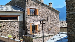 A stone building with a balcony, a window with wooden shutters, and a small outdoor seating area. - I Sitoù - Ratizin Apartment: The Scent of Ancient Wood (Ostana)