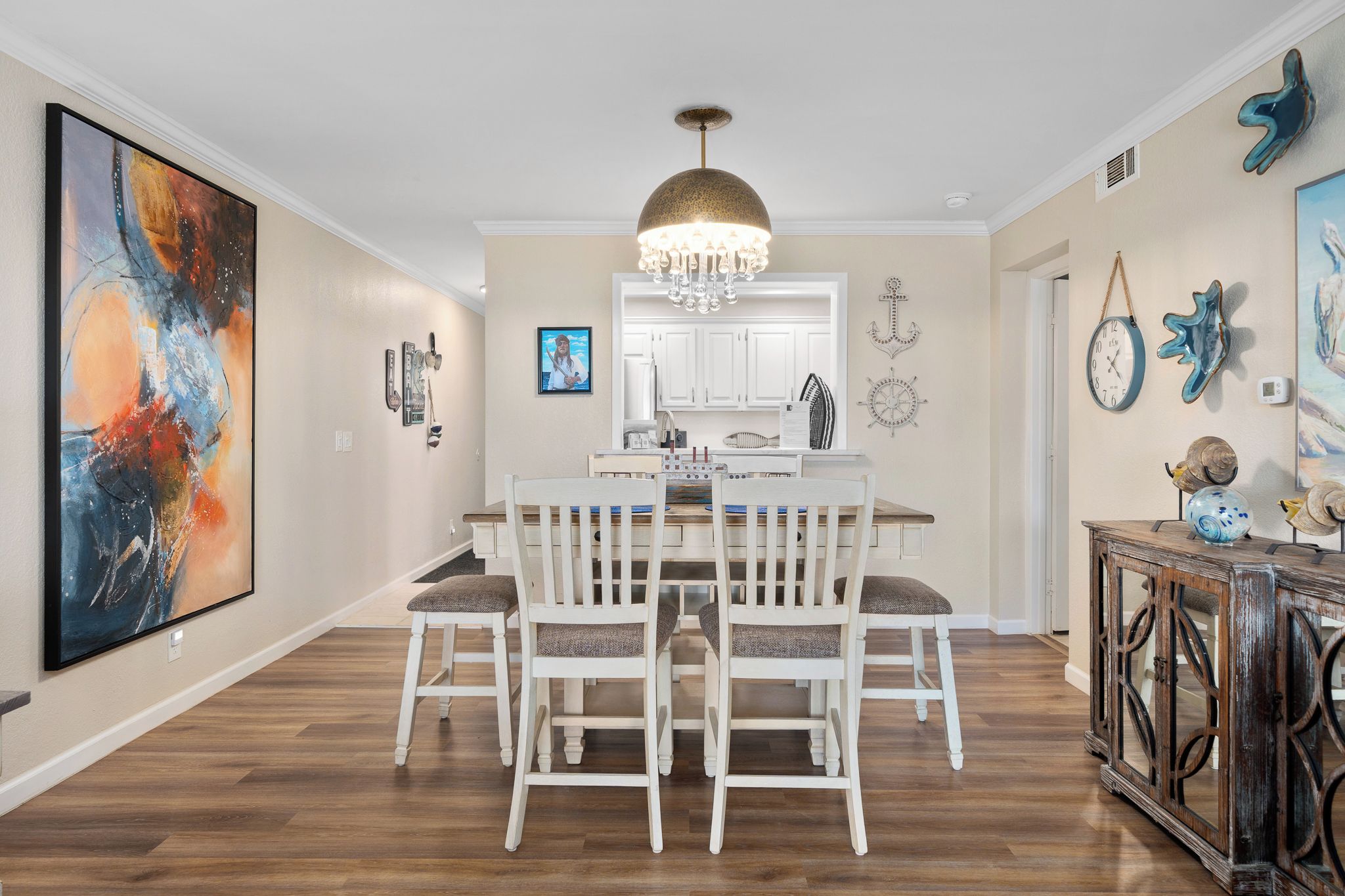 Un coin repas avec une table et des chaises blanches, un lustre et un grand tableau abstrait accroché au mur.