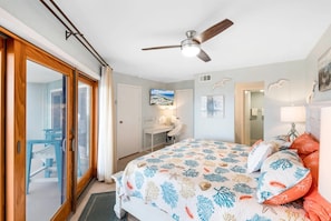 Ein Schlafzimmer mit Bett, Deckenventilator, Fernseher und Blick auf einen Balkon.